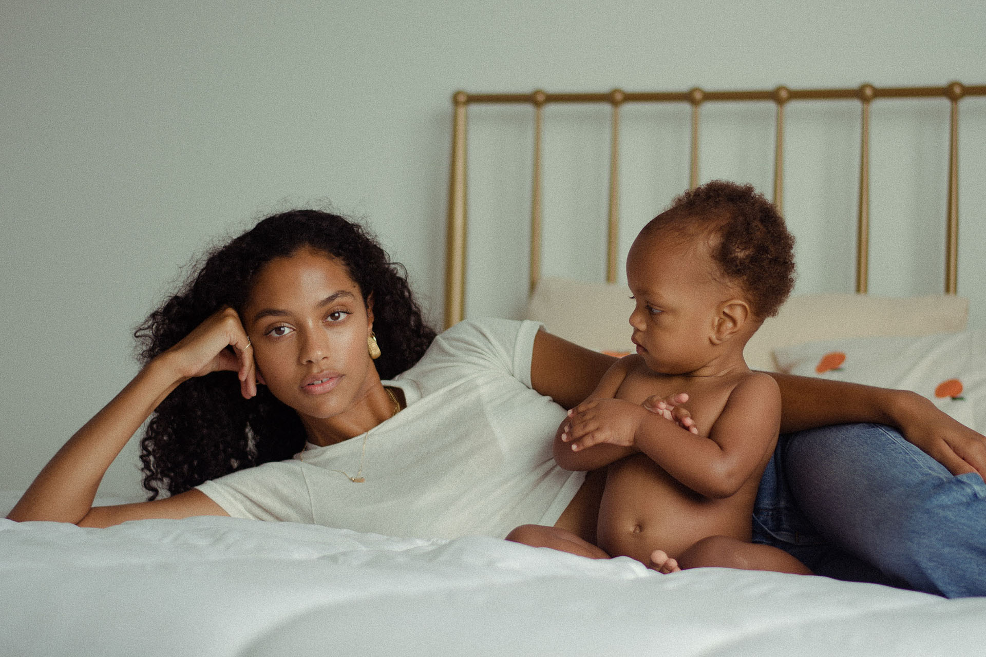 Mother laying on bed with her baby sitting beside her.